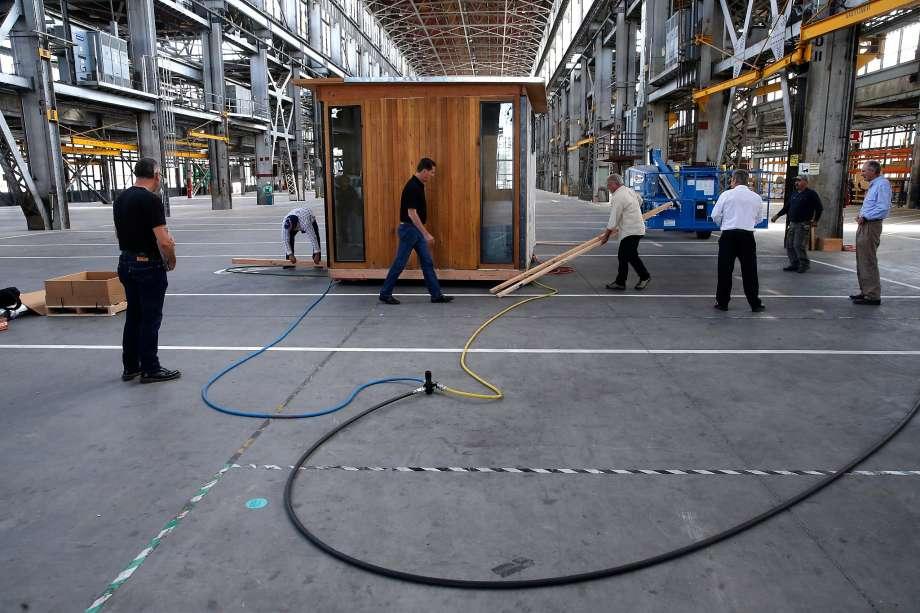 Workers assembling a small wooden room inside a large industrial warehouse
