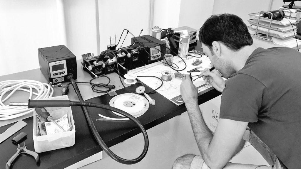 Person soldering electronics at a cluttered workbench