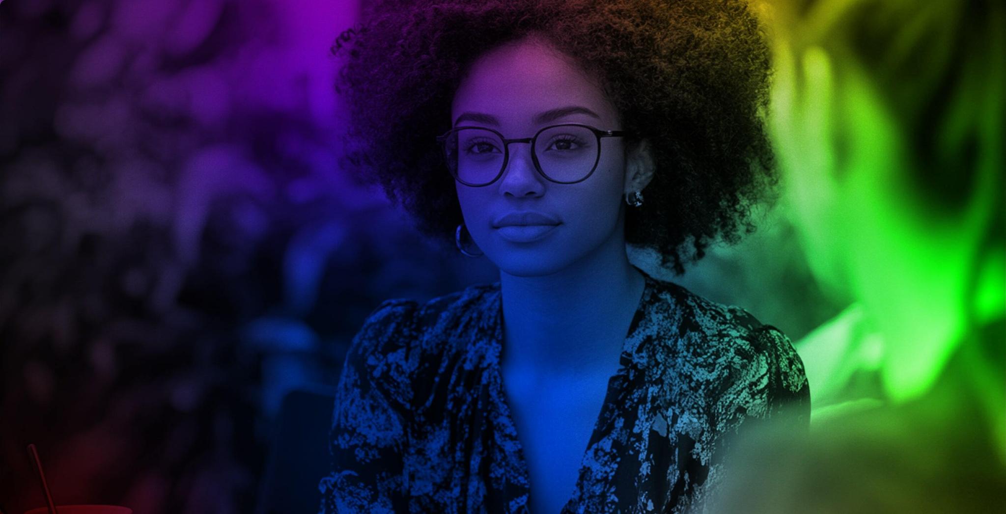 Woman with glasses lit by purple, blue, and green neon colors