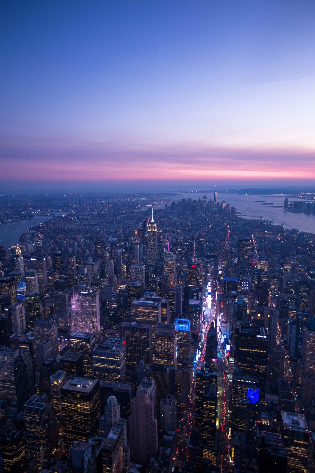 Aerial view of New York City at dusk with lit skyscrapers and river