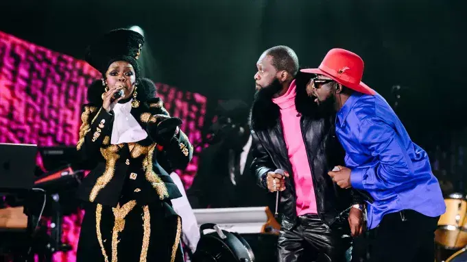 Three performers singing onstage in colorful outfits