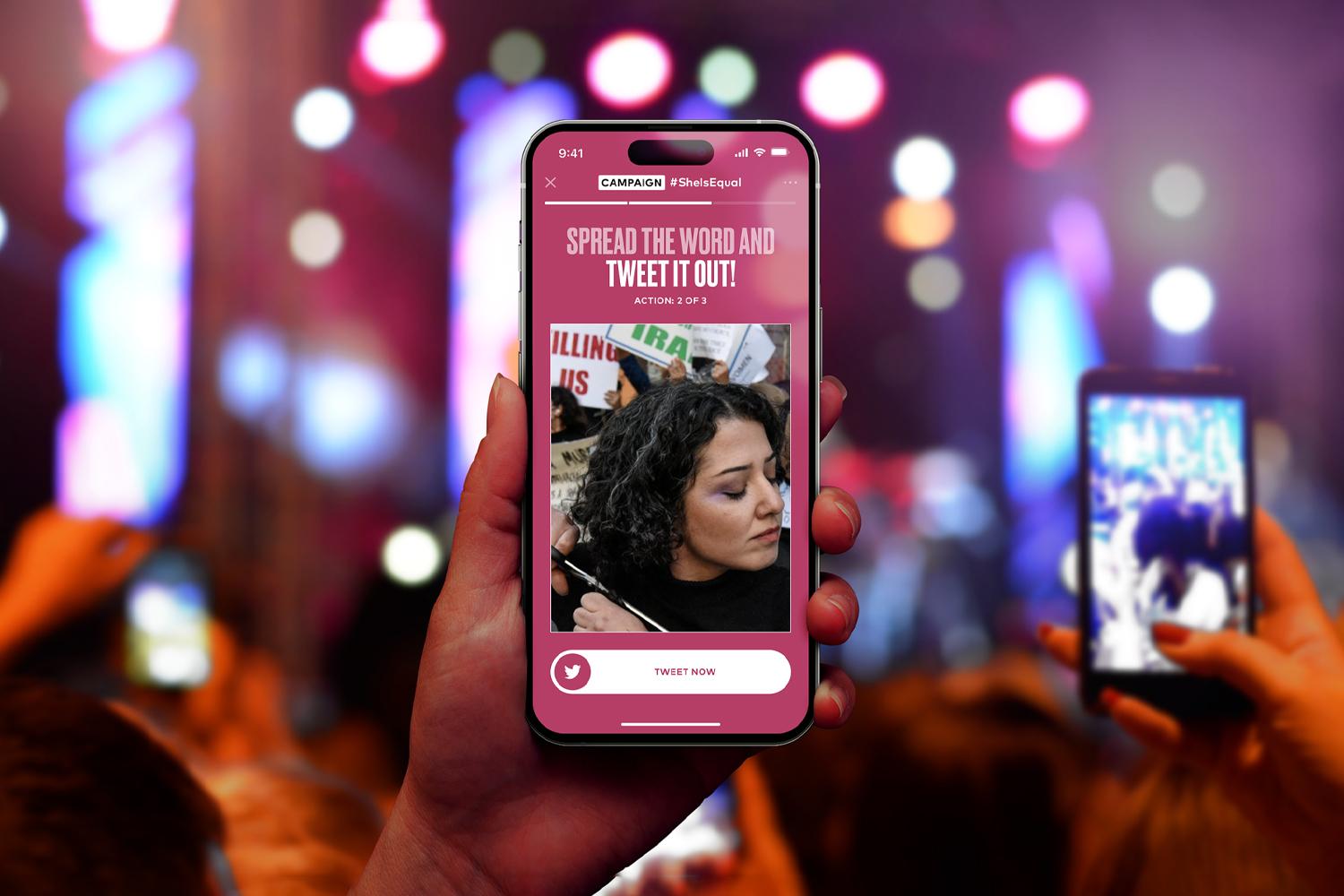 Hand holding a phone showing a social campaign page at a concert or rally with blurred lights in the background