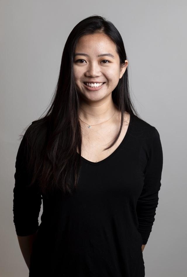 Smiling woman in a black top standing against a gray studio background.