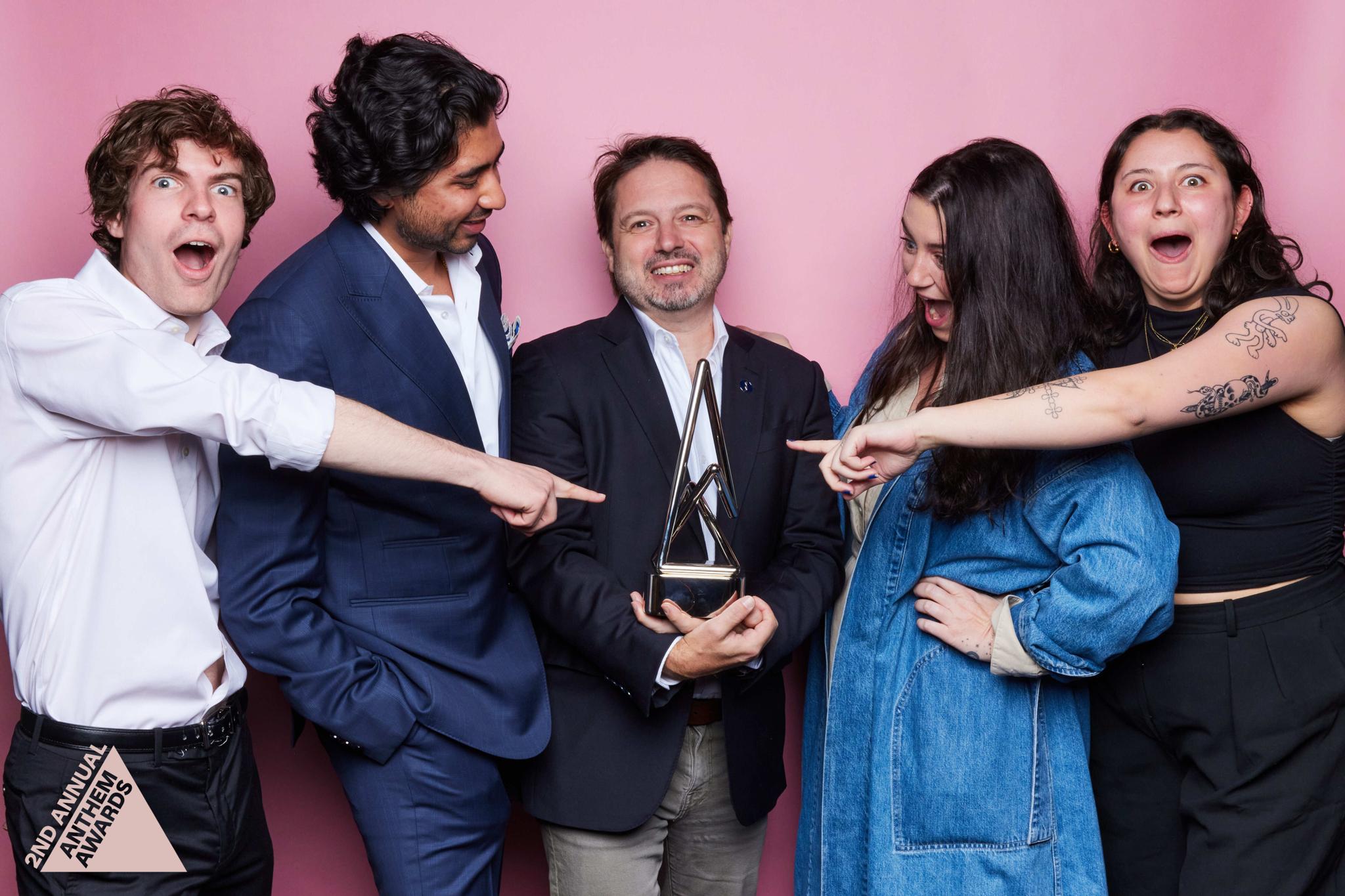 Group of five posing playfully with an Anthem Awards trophy
