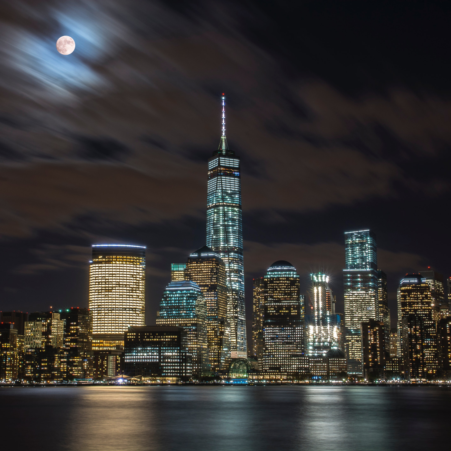 Lower Manhattan skyline at night with One World Trade Center and a full moon