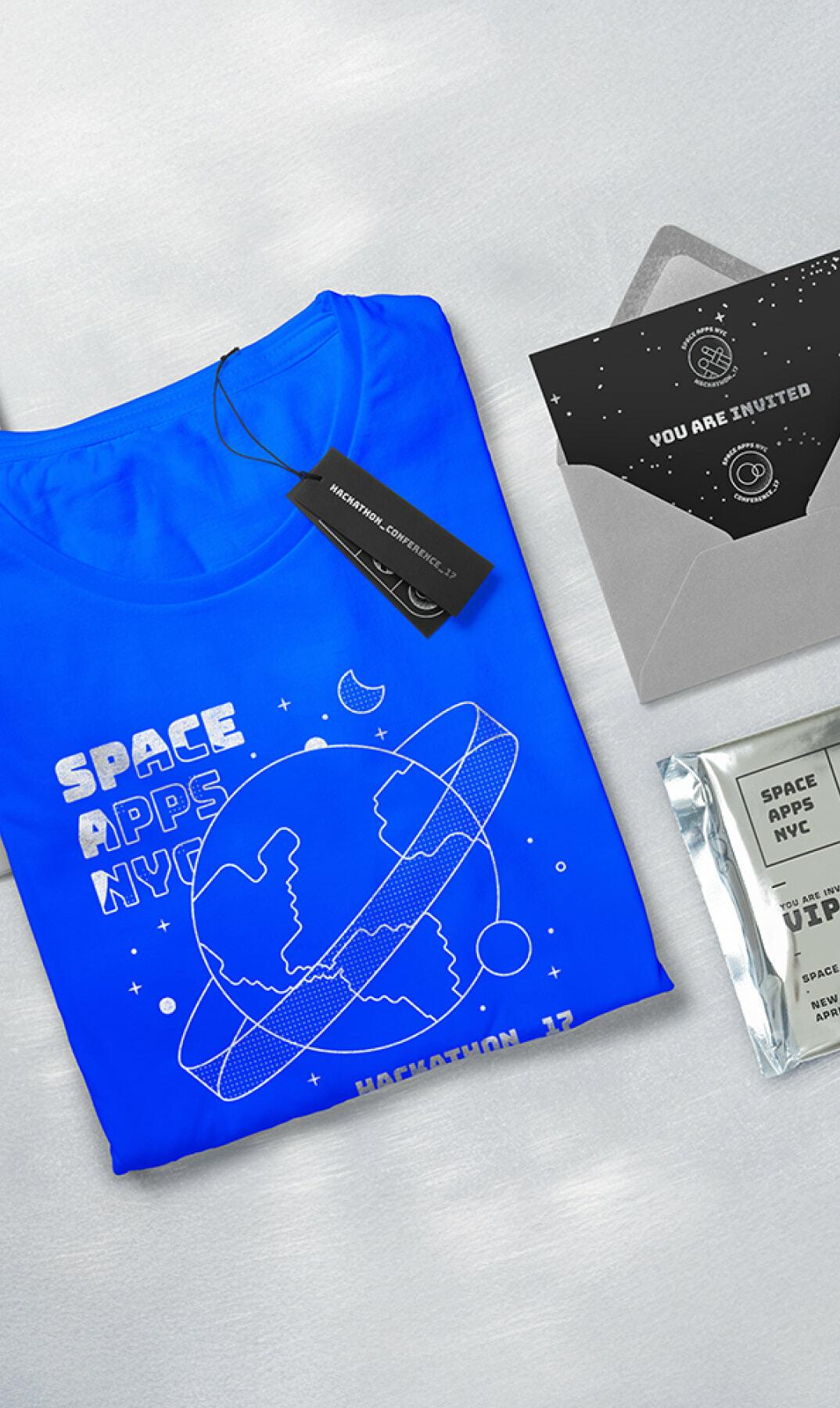 Blue Space Apps NYC T-shirt with invitation cards, envelope, and sticker on a table
