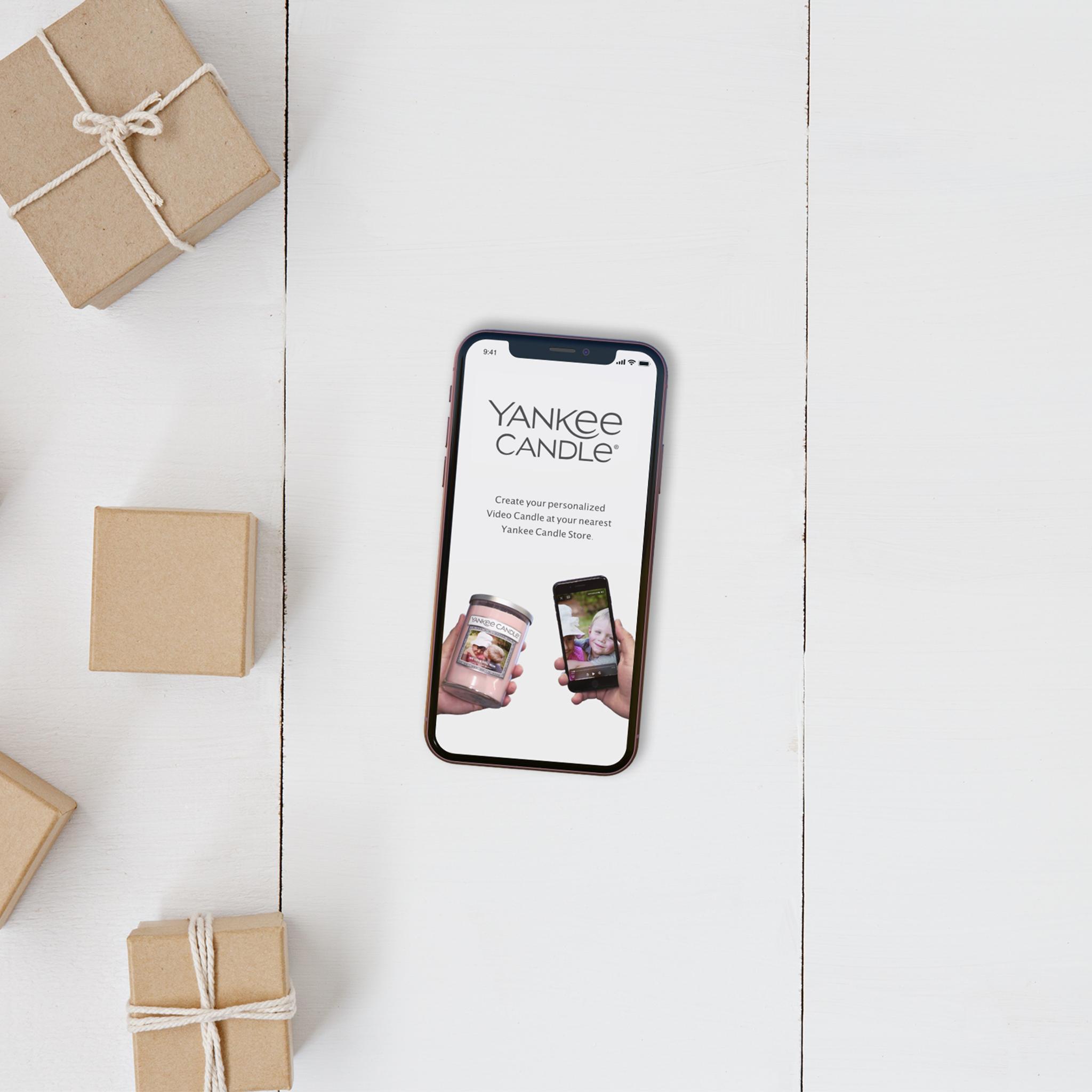 Phone showing a Yankee Candle page on a white table with wrapped boxes