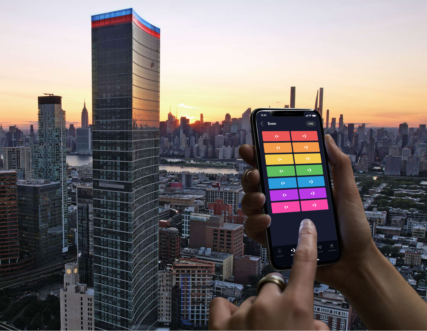 Hand using a colorful phone app against a New York City skyline at sunset