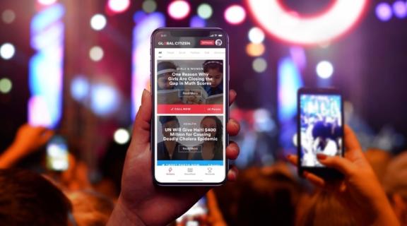 Hand holding a phone with Global Citizen app open in a concert crowd