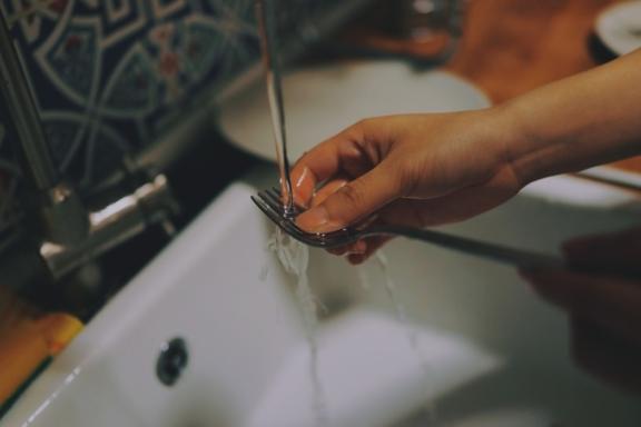 Hand rinsing a fork under running water in a sink