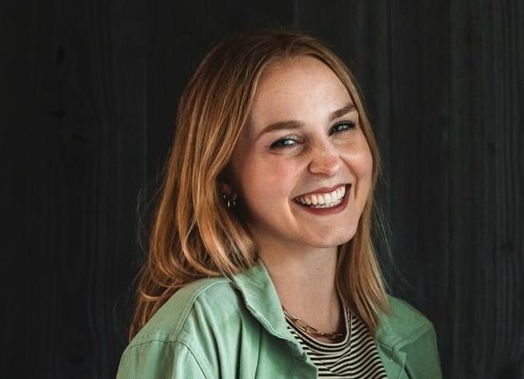 Smiling woman in green jacket against a dark wood wall