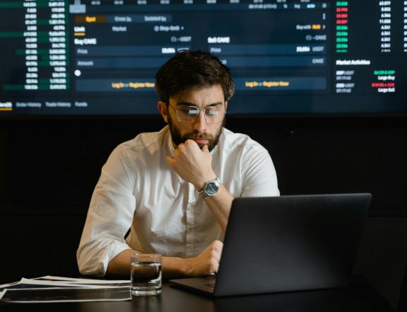 Man using a laptop in front of large financial trading screens