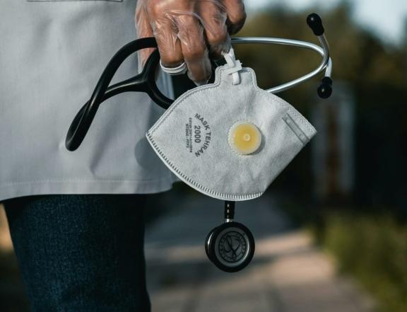 Hand holding an N95 mask and stethoscope outdoors