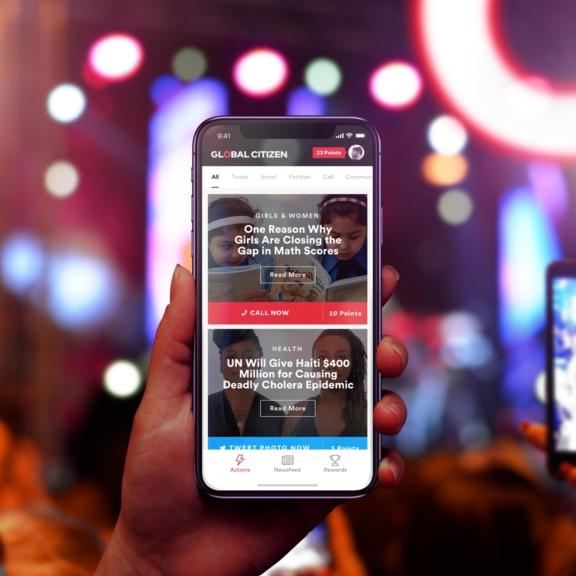 Hand holding smartphone showing the Global Citizen app against colorful blurred lights