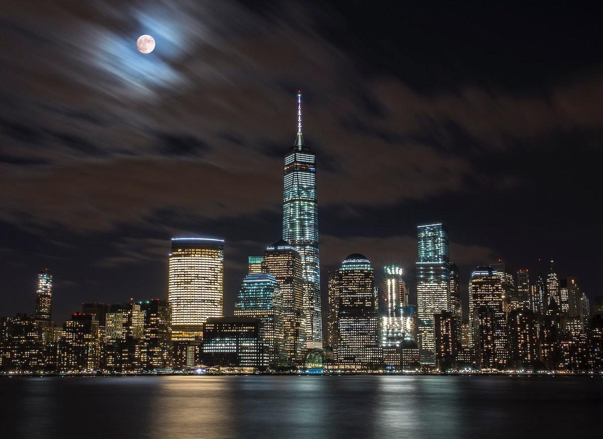 New York City skyline at night with One World Trade Center and a cloudy moon