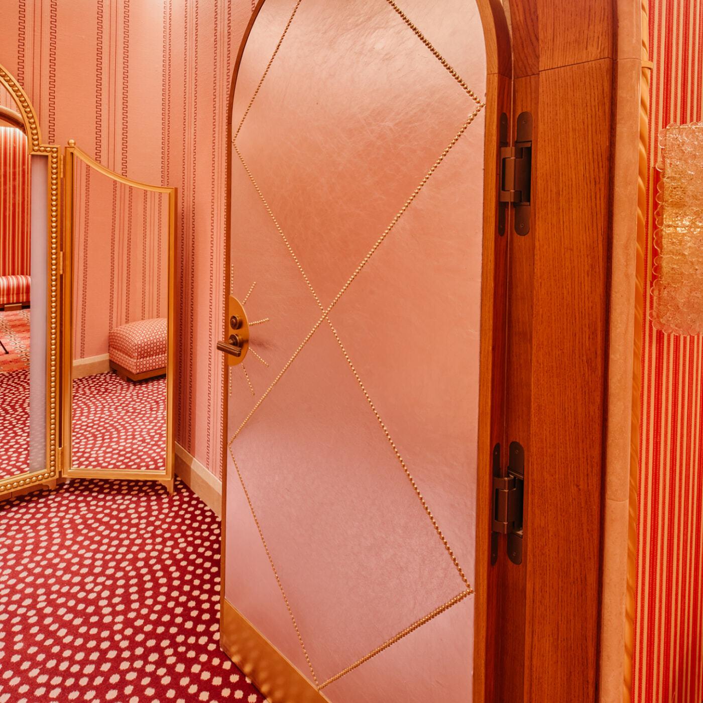 Pink arched door opening into a red and pink patterned fitting room