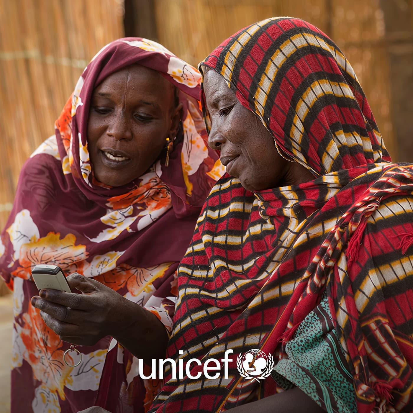 Two women in patterned headscarves looking at a phone, with UNICEF logo