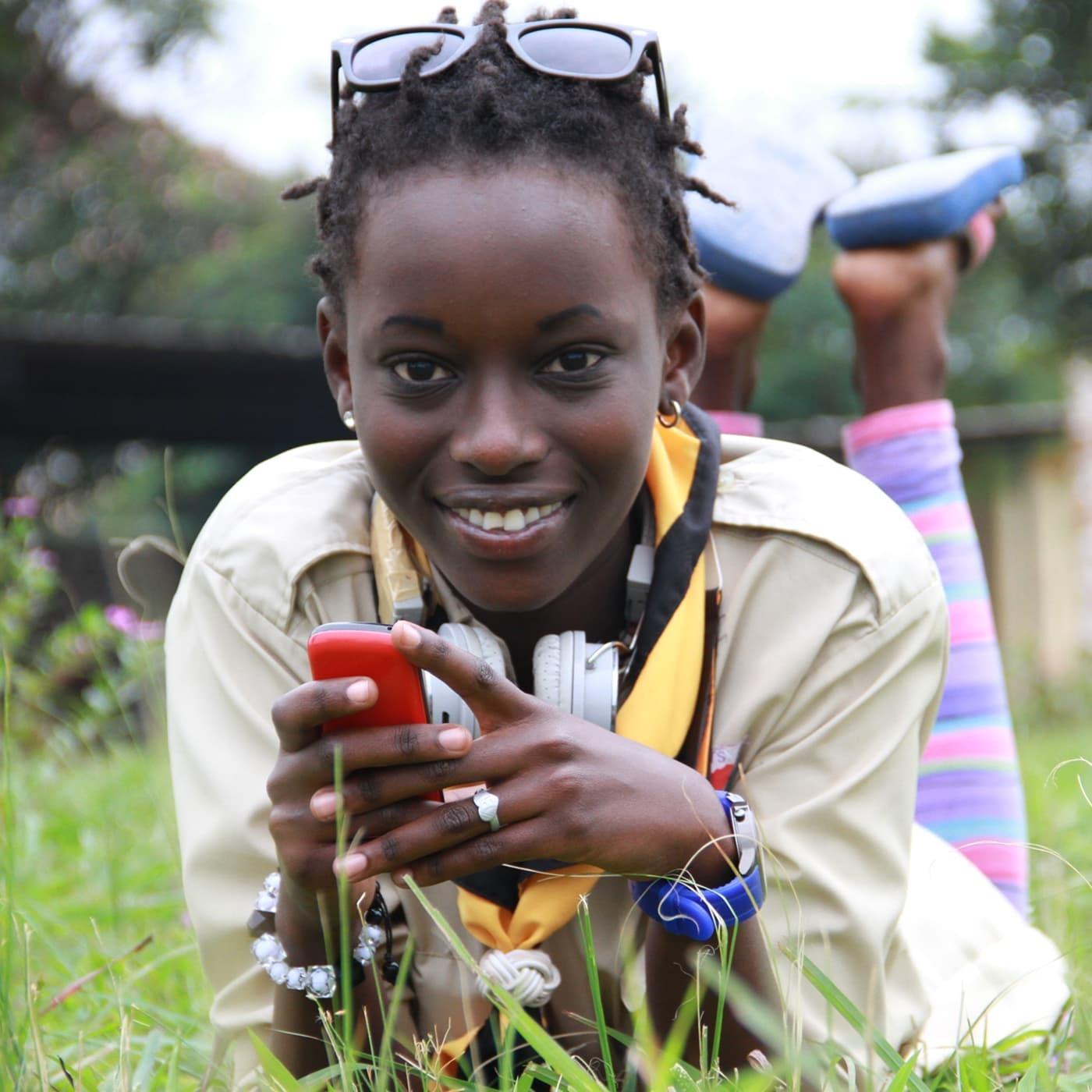 Smiling young woman lying in grass holding a red phone