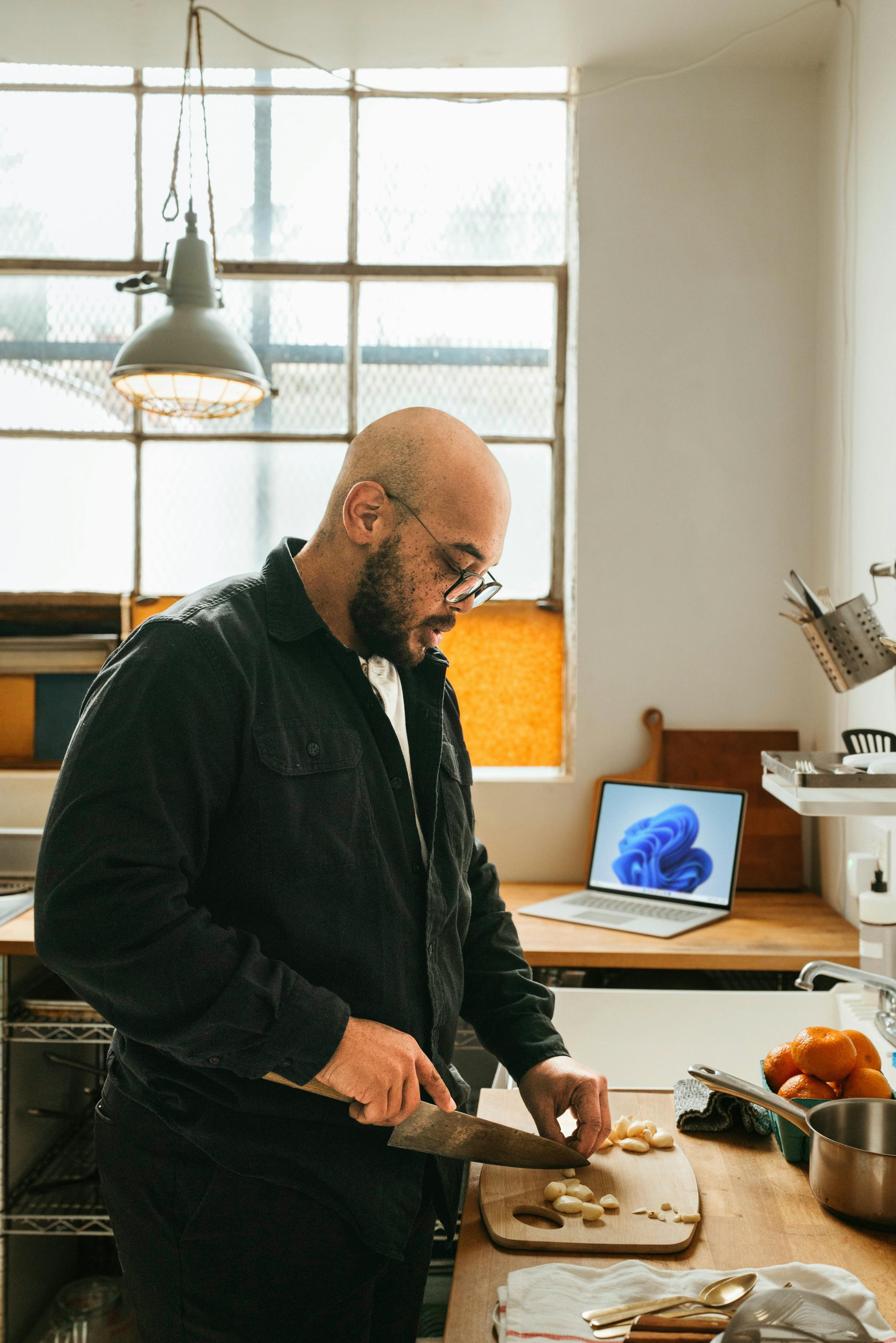 Person chopping garlic on a cutting board in a sunlit kitchen