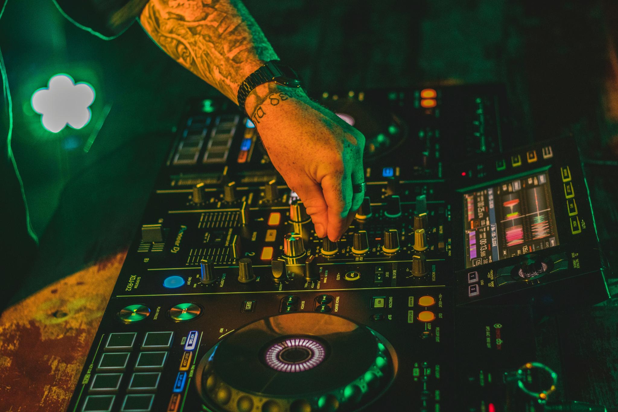 Hand adjusting a DJ mixer under green club lighting