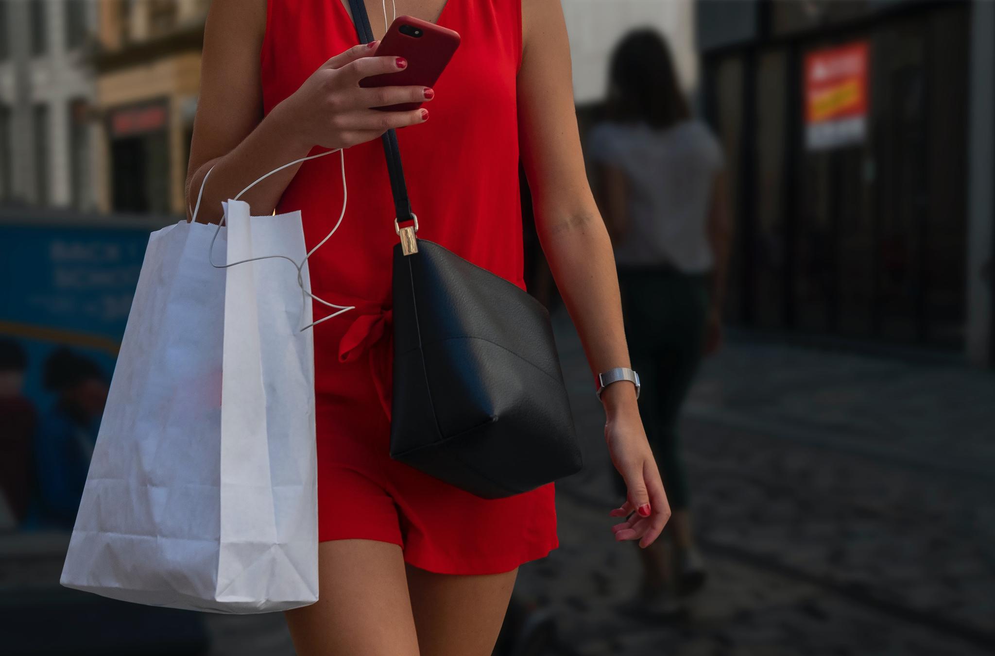 Person in red outfit holding a phone and shopping bags
