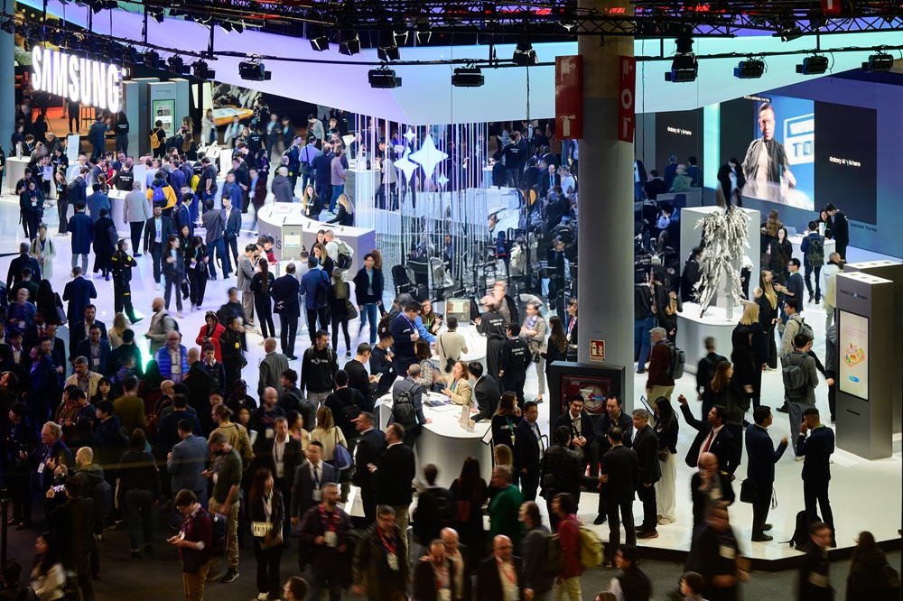 Crowded Samsung trade show booth with large displays, product demos, and attendees networking indoors