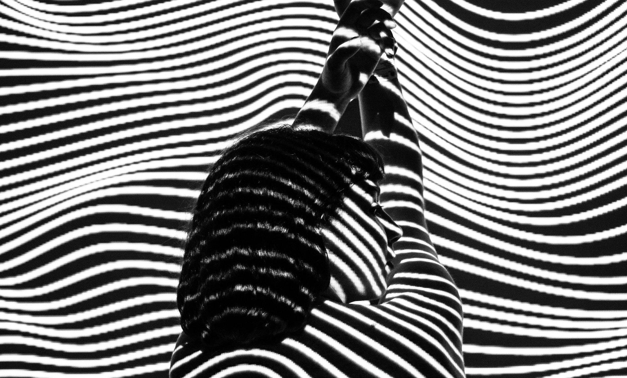 Person silhouetted against wavy black-and-white projection lines