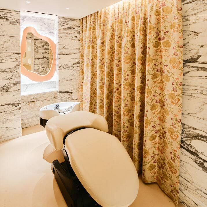 Beauty treatment chair in a marble-walled room with floral curtains and a sink