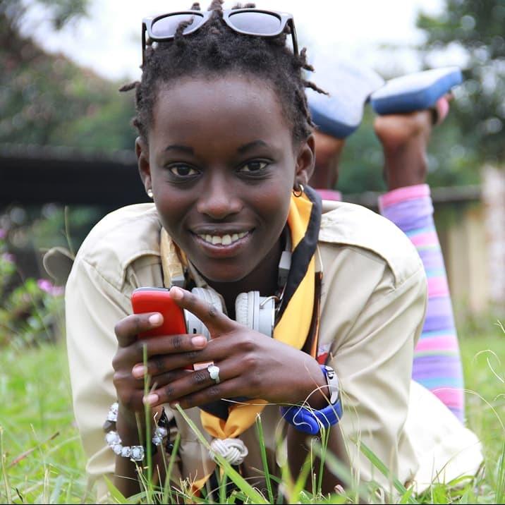 Smiling young woman lying in grass holding a red phone