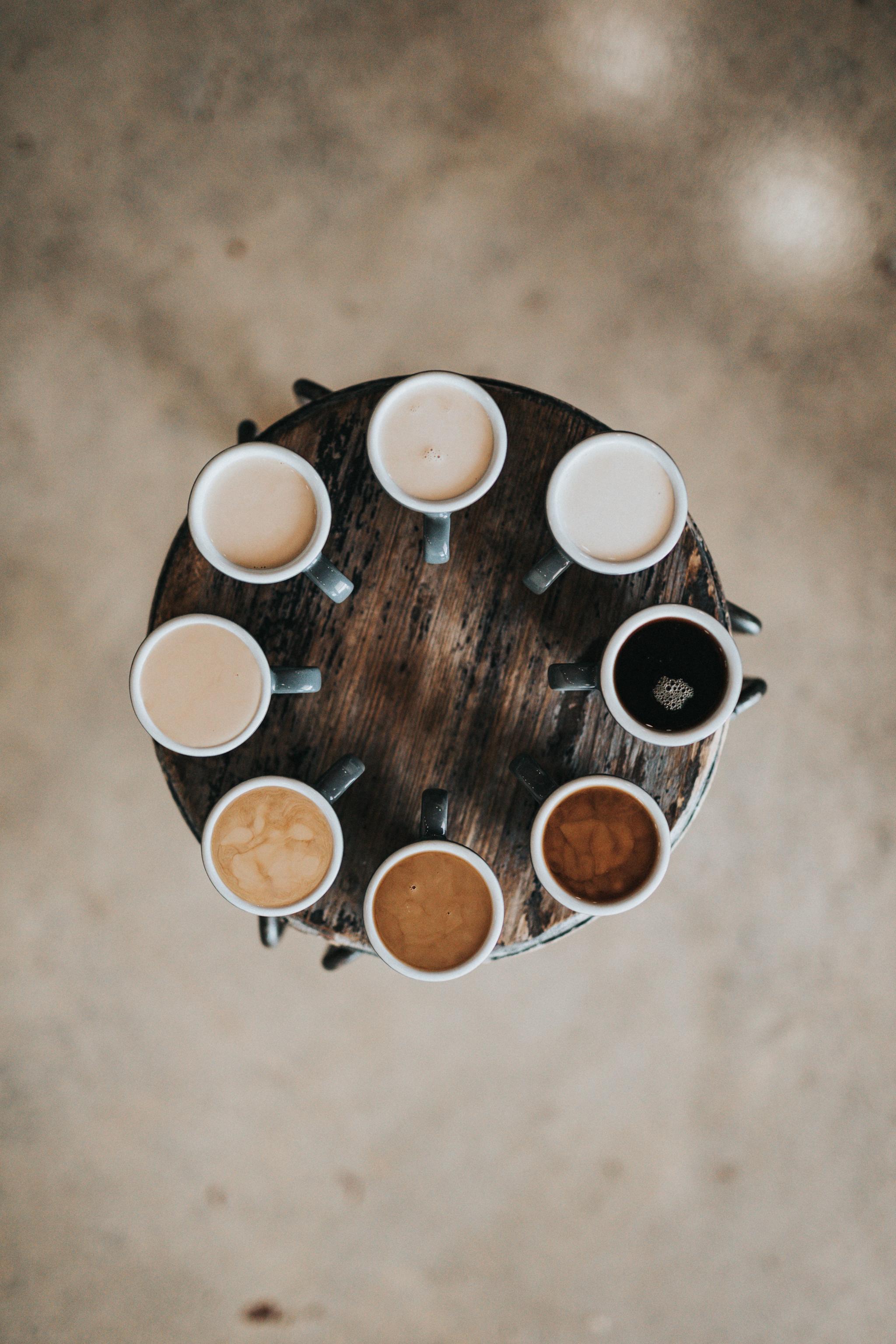 Eight mugs of coffee arranged around a small round wooden table