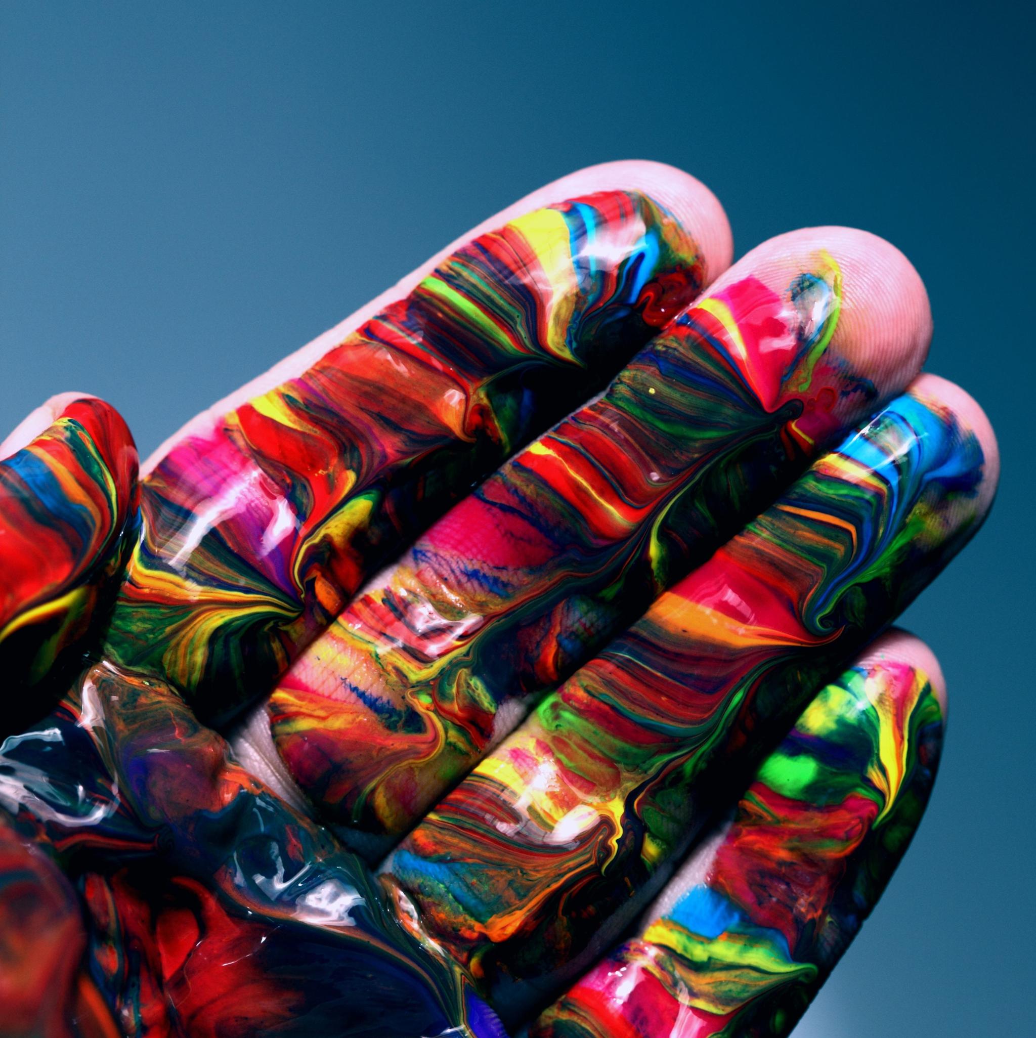 Hand covered in glossy multicolored paint against a teal background