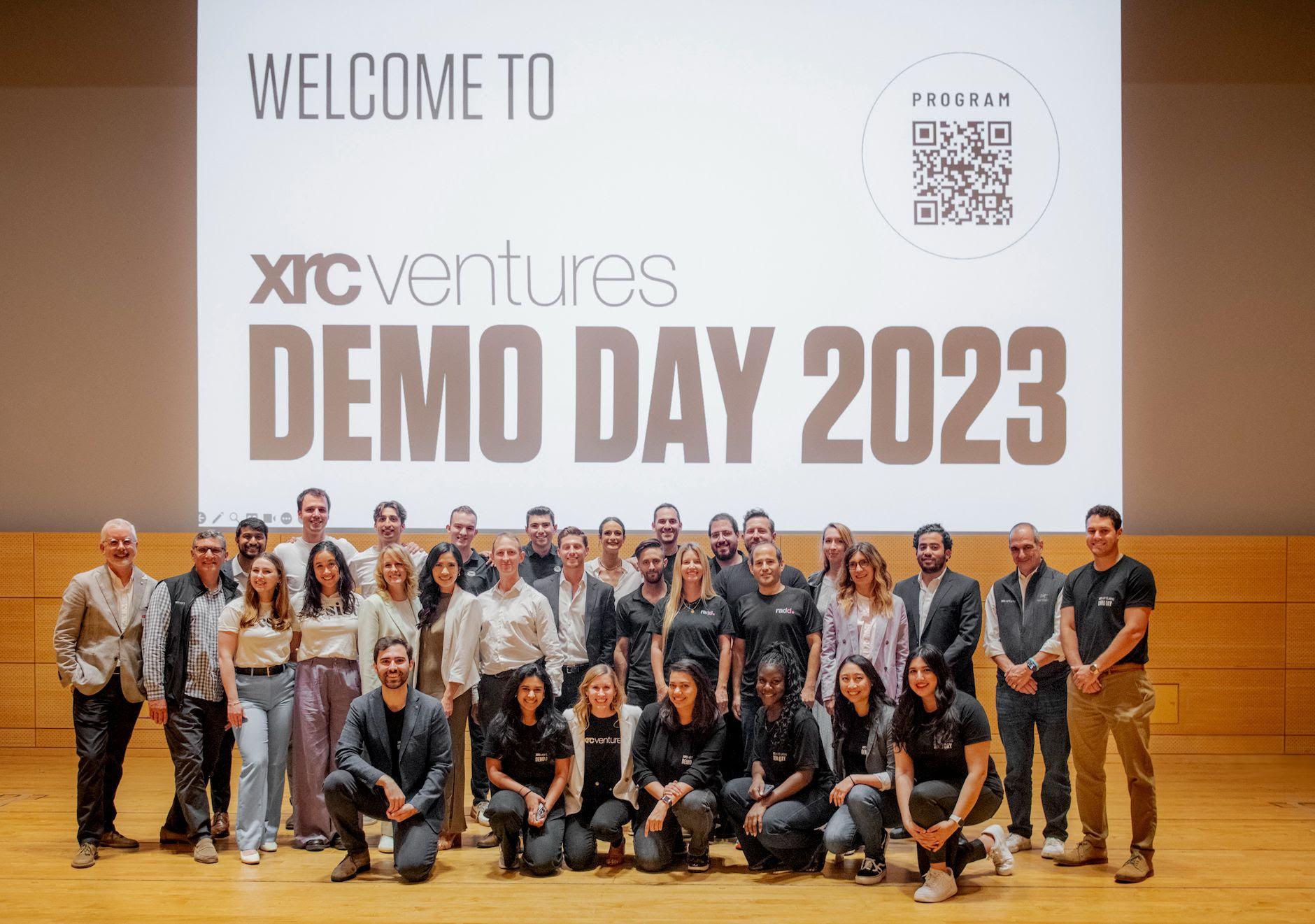 Group posing on stage below xrcventures Demo Day 2023 screen