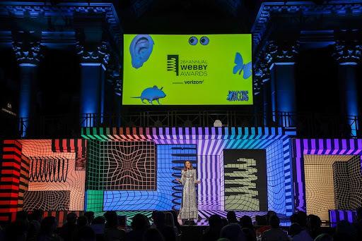 Webby Awards stage with presenter, colorful patterned set, and audience