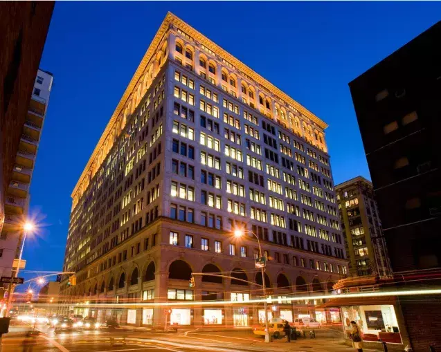 Lit brick-and-terracotta office building on a Manhattan corner at dusk, traffic streaking past