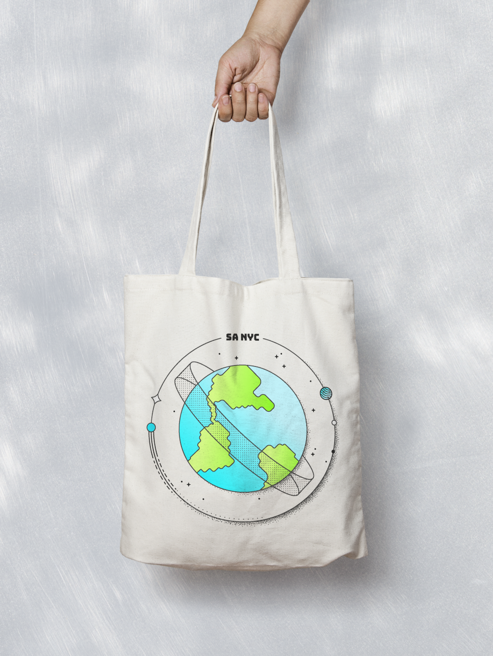 Hand holding a canvas tote bag with an illustrated planet design