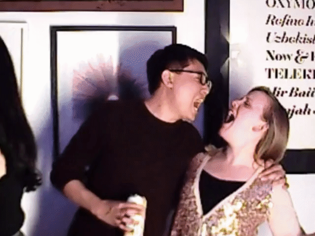 Two people laughing with arms around each other in an indoor setting