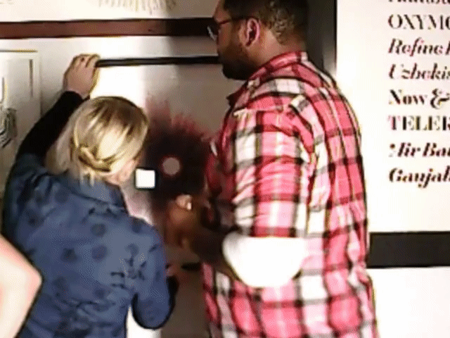 Two people standing by a doorway, one in a red plaid shirt and one with blond hair