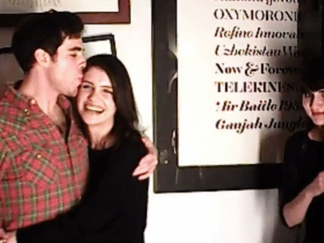 Young man kissing a smiling woman on the forehead at an indoor gathering