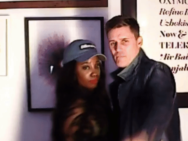 Two people posing together indoors in front of framed wall art