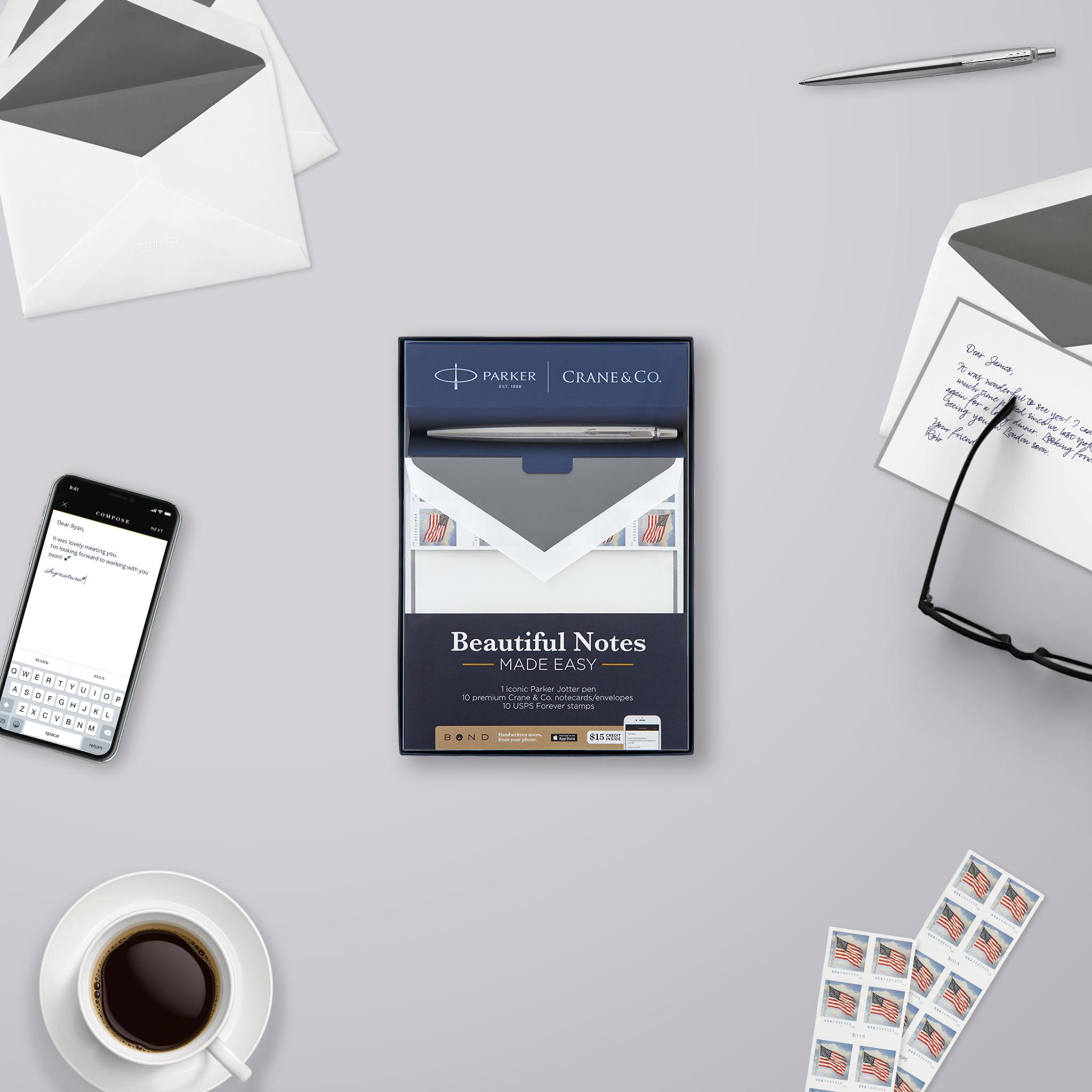 Desk flat lay with the Parker and Crane & Co. boxed set, a handwritten note, stamps and the Bond app