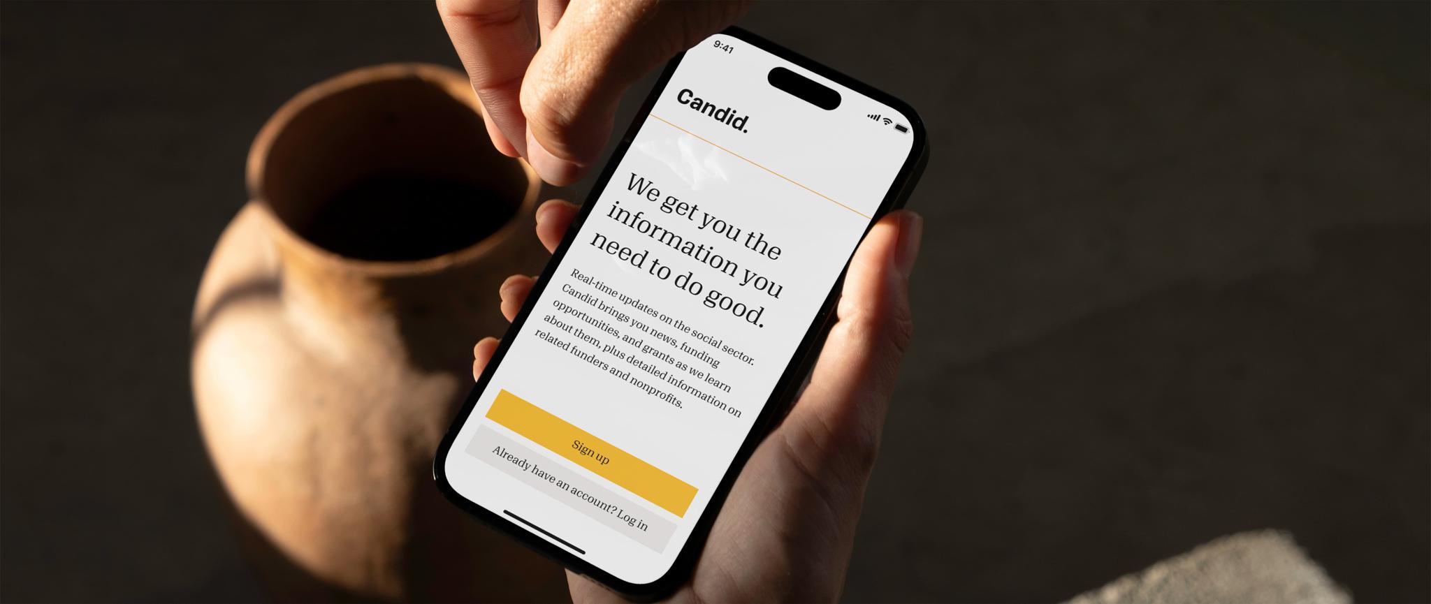 Phone with Candid sign-up page held near a ceramic cup