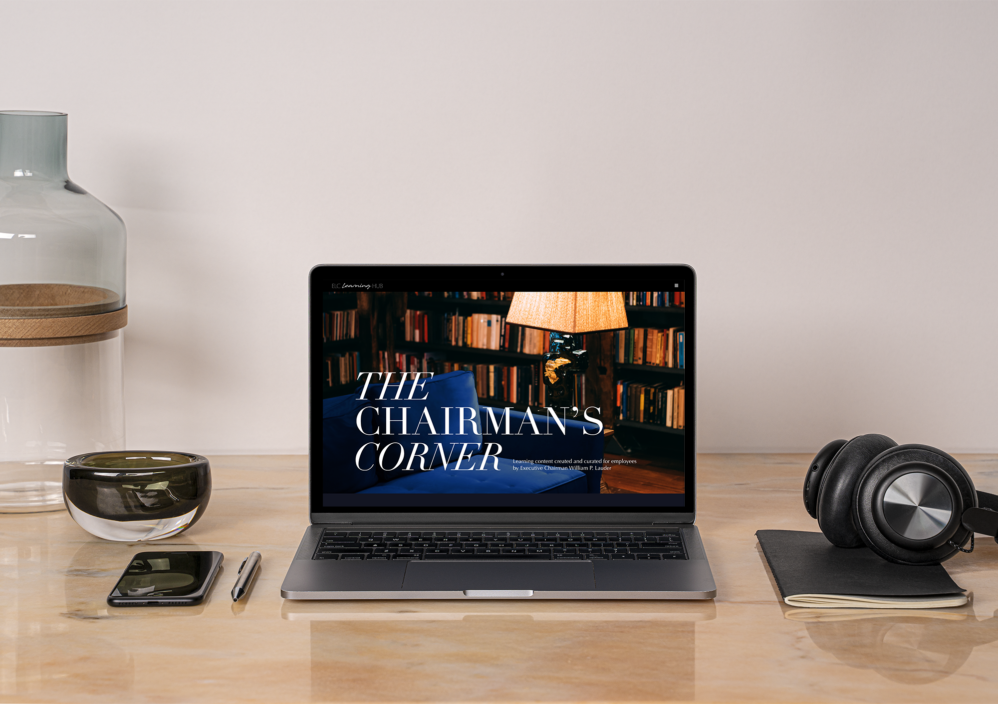 Laptop on a desk showing The Chairman's Corner, with headphones and office items