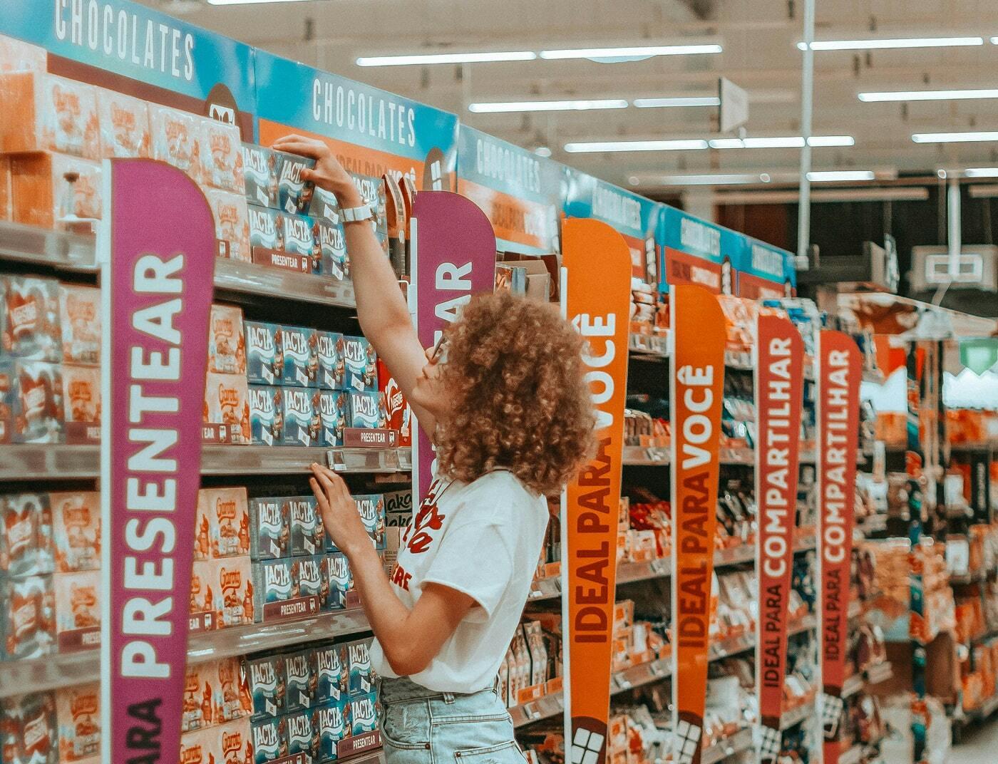 Shopper reaching for chocolate boxes in a brightly signed retail aisle