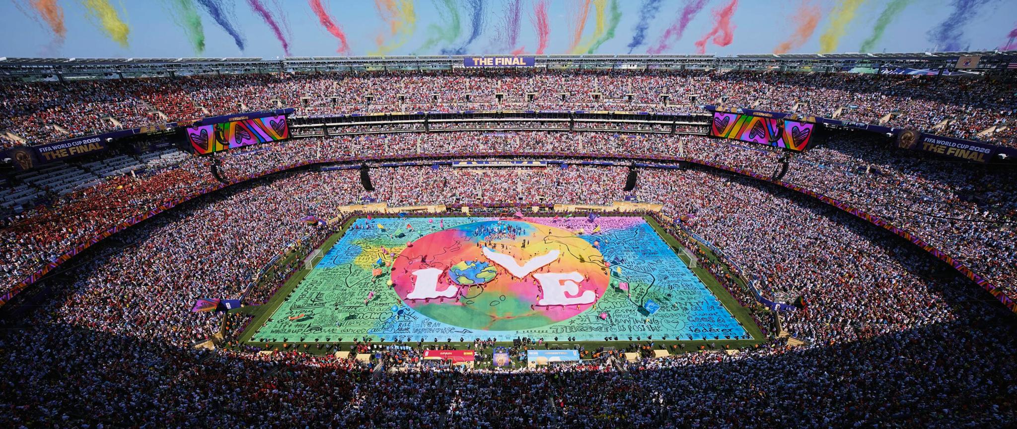 Packed stadium with a colorful Believe in Love display on the field.
