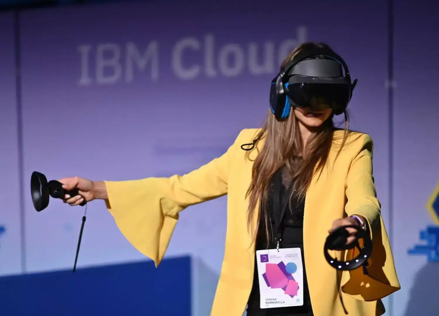 Person in yellow blazer using VR headset and controllers at an IBM Cloud event