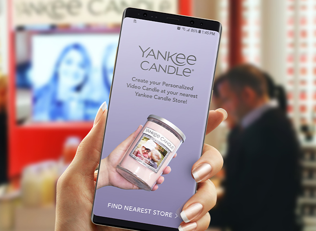 Hand holding a phone with a Yankee Candle personalization app in a store