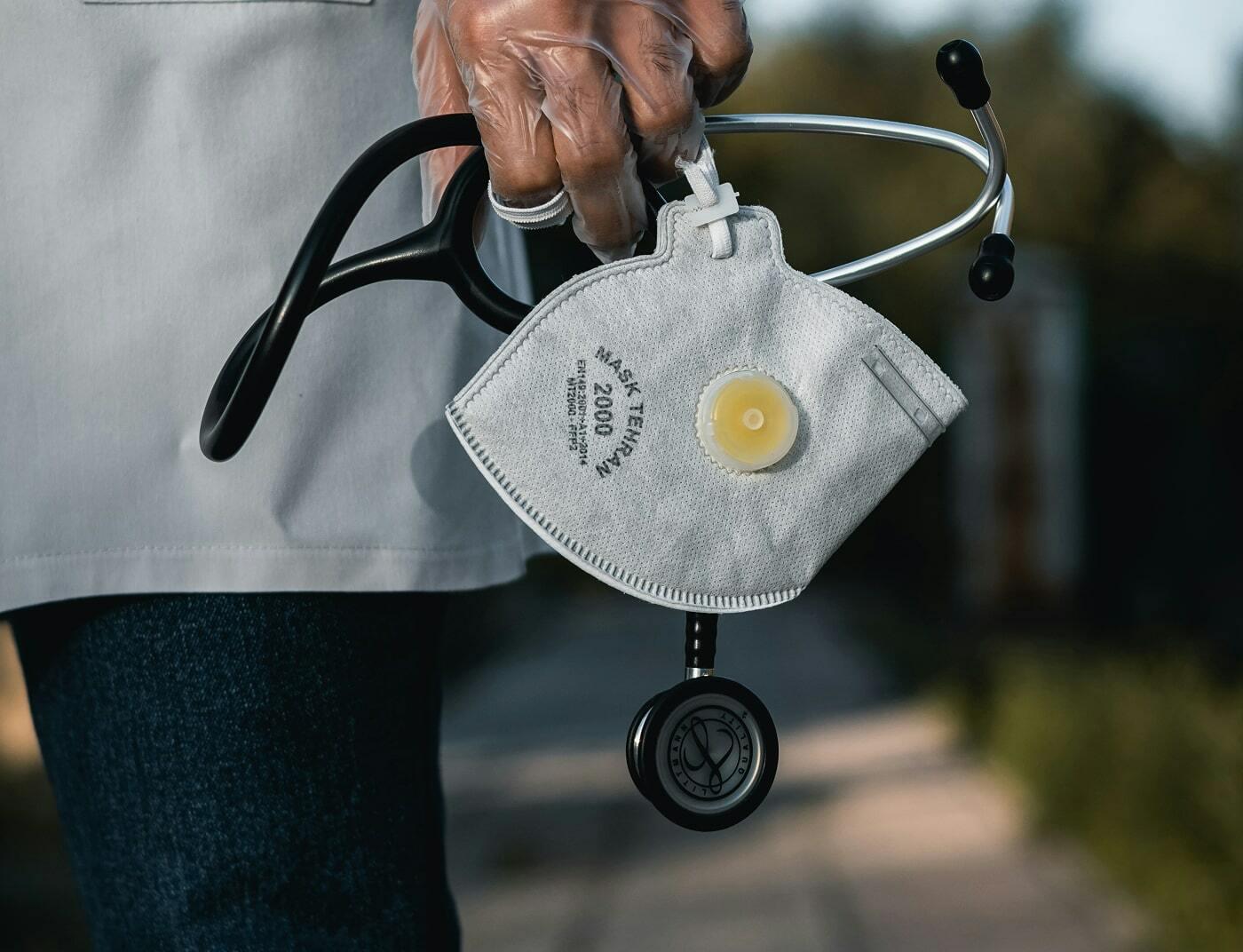 Hand holding an N95 mask and stethoscope outdoors