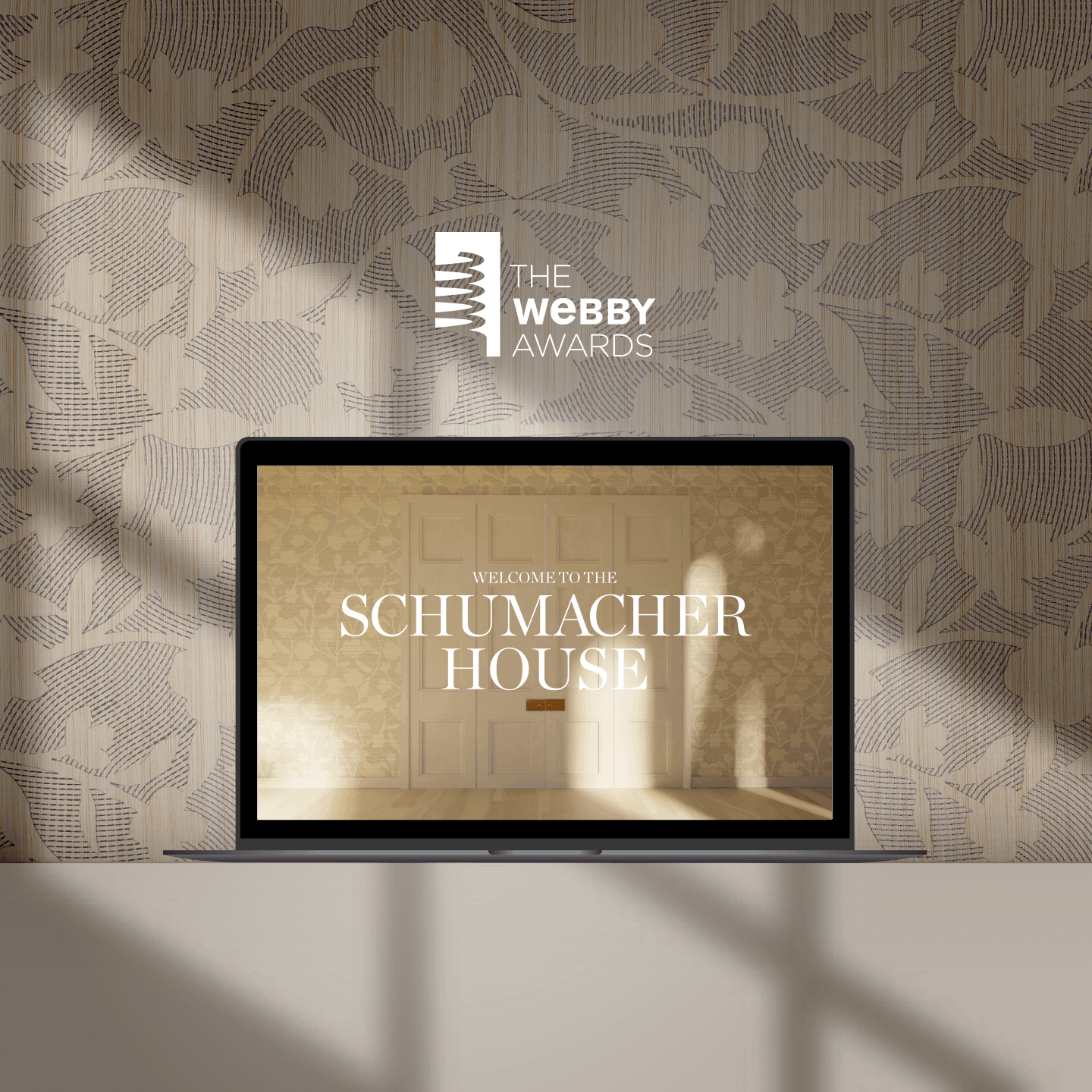 Laptop showing Schumacher House website in front of patterned wallpaper and Webby Awards logo