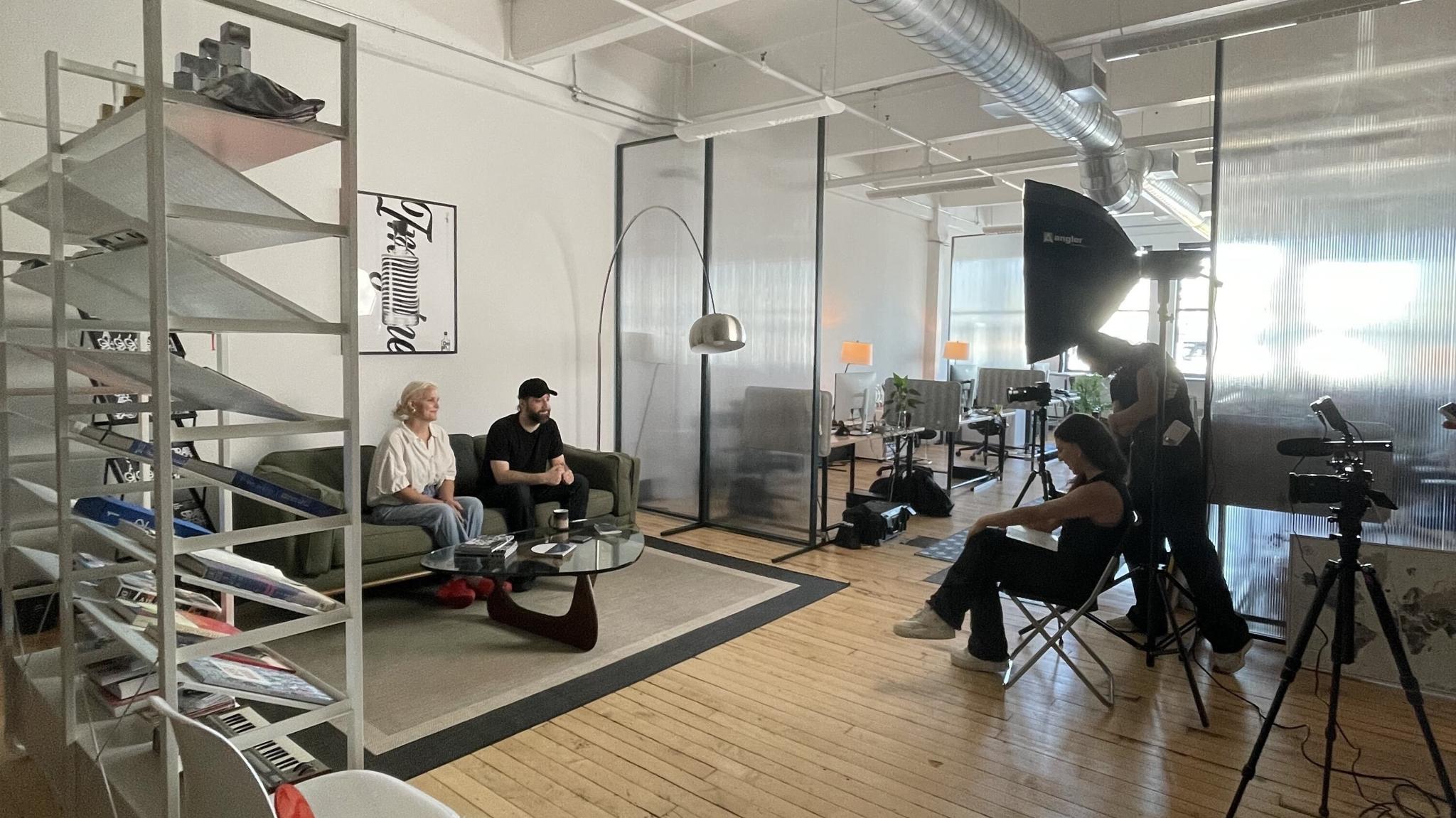 Camera crew filming an interview with two L+R team members on a sofa in the studio's office