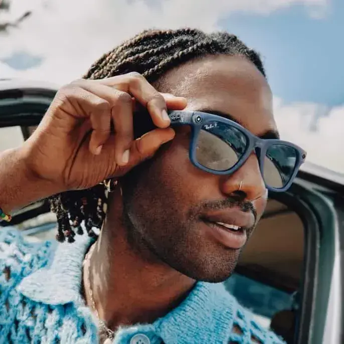 Man lifting blue Ray-Ban Meta smart glasses while leaning out of a car window